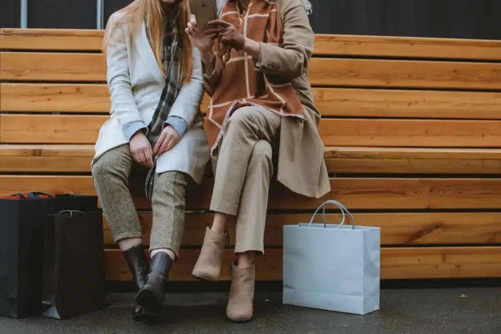 Two people sit with shopping bags, looking at a smartphone. 