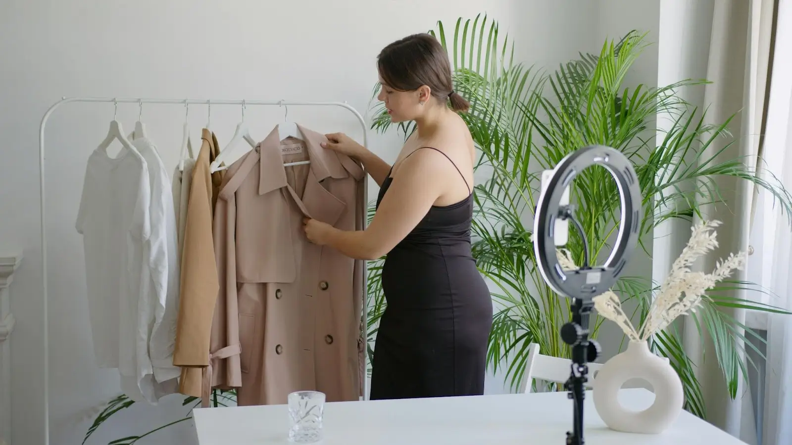A fashion influencer films a video, showing a trench coat to her audience.